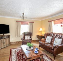 A living room with leather chairs wooden coffee table television and patterned rug at Frongoch Cottage in Red Wharf Bay near Pentraeth