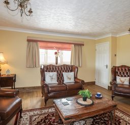 A living room with leather armchairs a wooden coffee table and a window with curtains at Frongoch Cottage Red Wharf Bay near Pentraeth