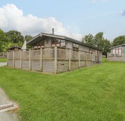 Two wooden lodges with fenced decks on a grassy area with trees in the background at Rivendell Lodge in Roger Ground near Hawkshead