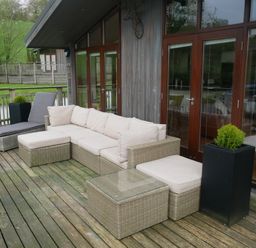 An outdoor deck with wicker furniture including a sofa chaise lounge and table at Rivendell Lodge Roger Ground near Hawkshead