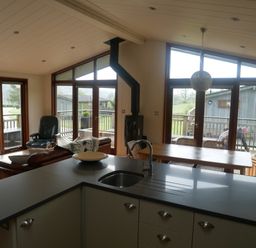A kitchen island with a sink and faucet overlooking a dining table and living area with large windows and wooden doors at Rivendell Lodge in Roger Ground near Hawkshead
