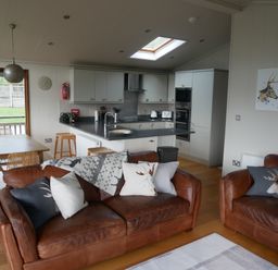 A living room with brown leather sofas and cushions beside a kitchen with cabinets and a dining table at Rivendell Lodge in Roger Ground near Hawkshead