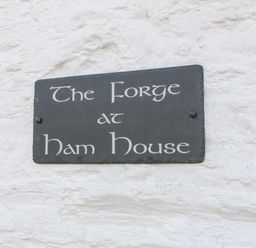 A black sign with white text on a white textured wall at The Forge in Taunton