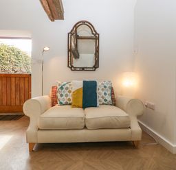 A beige sofa with cushions against a white wall with a decorative mirror above at The Forge in Taunton