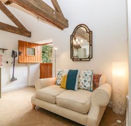 A small sitting area with a beige sofa and colorful cushions under exposed wooden beams at The Forge in Taunton