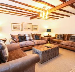 A living room with two brown sofas a wicker coffee table and wooden ceiling beams at Well Cottage in Grimston