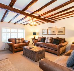 A living room with brown sofas a wicker coffee table wooden ceiling beams and framed pictures on the wall at Well Cottage Grimston