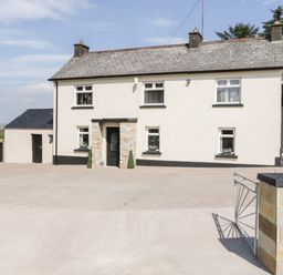 A two-story stone farmhouse with a front door and multiple windows with flower boxes and a paved driveway at Peters Farmhouse in Cookstown
