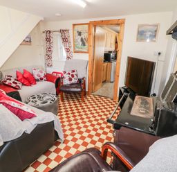 A living room with sofas red and white cushions a black stove a TV and a wooden doorway leading to a kitchen at Peters Farmhouse in Cookstown