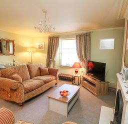 A living room with a patterned sofa a coffee table with fruit a television on a stand and a fireplace at Drake's Retreat in Plymouth