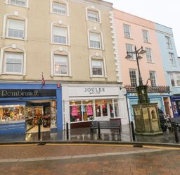 Three story buildings with shops on the ground floor benches and a street lamp in front of them at Gower View in Tenby