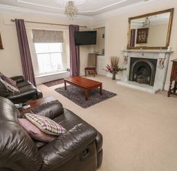 A living room with leather sofas a wooden coffee table a fireplace and a wall-mounted TV at Gower View in Tenby