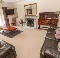 A living room with leather sofas a wooden coffee table a fireplace a large mirror and a wooden sideboard at Gower View in Tenby