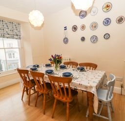 A dining room with a window six wooden chairs a table set with plates and glasses and decorative plates on the wall at Gower View in Tenby