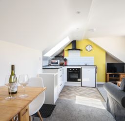 A kitchen and living area with a small dining table bottle of wine and two wine glasses at Ayla in Lyme Regis