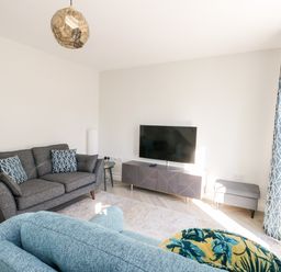 A living room with a grey sofa, blue armchair, TV on a stand, and blue patterned curtains at 3 Trem Y Dolydd Dolgarrog near Llanrwst