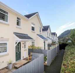 A row of beige two story houses with slate roofs and green doors along a narrow paved path with wooden fences and shrubbery at 3 Trem Y Dolydd in Dolgarrog near Llanrwst