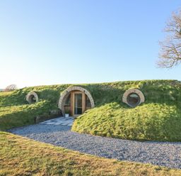 A small earth house with a grass roof and circular windows at Tan y Wawr- Onnen in Llanfair Caereinion