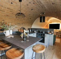A kitchen with a curved brick ceiling wooden stools and a living area with a TV at Tan y Wawr Onnen Llanfair Caereinion