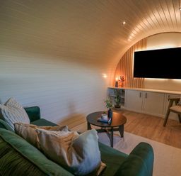 A living room with a green sofa white pillows a round black coffee table a wooden chair and a wall mounted television at Tan y Wawr- Onnen in Llanfair Caereinion