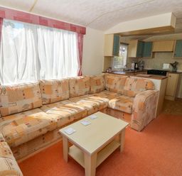 A living room with a patterned corner sofa and coffee table next to a small kitchen at Gorphwysfa Caravan in Tregele near Cemaes Bay