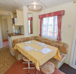 A dining area with a table covered by a yellow tablecloth and seating in a caravan at Gorphwysfa Caravan Tregele near Cemaes Bay