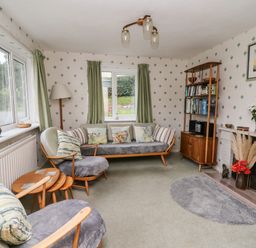 A sitting room with wooden furniture green curtains a fireplace and a bookshelf at Llwynon in Goginan near Aberystwyth