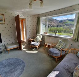 A living room with chairs and a sofa near a large window overlooking hills at Llwynon in Goginan near Aberystwyth