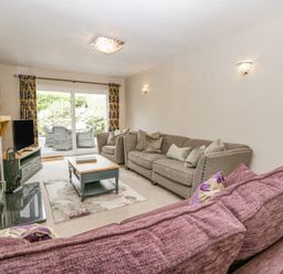 A living room with sofas a coffee table television and sliding glass doors leading to a patio at Holme Fell in Coniston