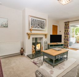 A living room with a wood stove fireplace a television on a stand a coffee table and sliding glass doors leading outside at Holme Fell in Coniston