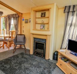 A living room with a fireplace a gray rug a television on a wooden stand a round dining table with chairs and a gray armchair at Rosehaven in Tegryn near Crymych