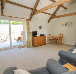 A living room with wooden beams a small dining table two chairs a TV on a wooden cabinet and sliding glass doors at The Parlour in Llangoedmor near Cardigan
