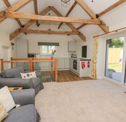 A living room with grey sofas and a kitchen with wooden beams on ceiling by sliding glass doors at The Parlour in Llangoedmor near Cardigan