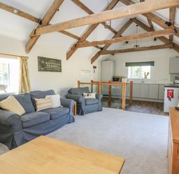 A living room with exposed wooden beams a blue sofa an armchair a wooden coffee table and a kitchen area at The Parlour in Llangoedmor near Cardigan