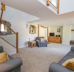 A living room with sofas pillows a plaid armchair a wooden cabinet with a tv a fireplace and flowers on a table at Cattle Tree Cottage in Llangoedmor near Cardigan