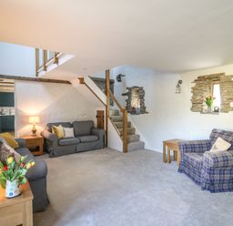 A living room with sofas a wooden side table stairs and exposed stone wall at Cattle Tree Cottage in Llangoedmor near Cardigan