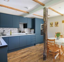 A kitchen with blue cabinets a white countertop a round dining table with wooden chairs and a vase of flowers at Cattle Tree Cottage Llangoedmor near Cardigan