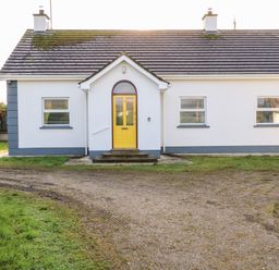 A single-story house with a yellow front door and three windows with blinds at 17 Buninver Road in Gortin