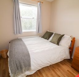 A bedroom with a bed with green pillows a grey blanket a wooden dresser and a window with curtains at 17 Buninver Road in Gortin