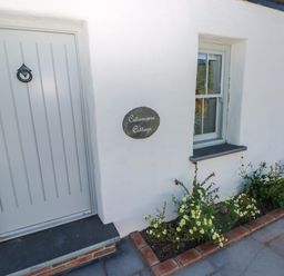 A white cottage exterior with a gray door a window and a flower bed at Catamouse in Milford Haven