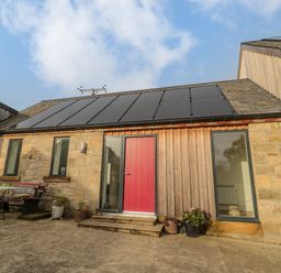 A stone and wood cottage exterior with solar panels on the roof a red door and patio furniture at High Barns Cottage in Longhorsley near Morpeth