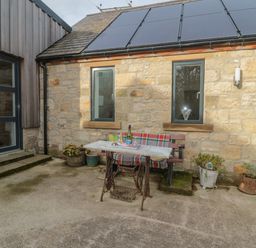 An outdoor patio area with an old sewing machine table and bench in front of a stone building with solar panels at High Barns Cottage Longhorsley near Morpeth