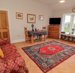 A living room with red patterned sofa yellow pillow wooden dining table chairs colorful rug wooden dresser and television at High Barns Cottage in Longhorsley near Morpeth