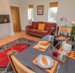 A dining area with a table set for breakfast and a red sofa in the background at High Barns Cottage in Longhorsley near Morpeth