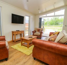 A living room with leather and fabric sofas a wooden coffee table a wall mounted tv and open doors to a deck at Robin Lodge in Gargrave