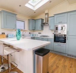A kitchen with blue cabinets a white island with two stools and appliances at Robin Lodge in Gargrave