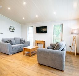 A living room with two grey sofas a coffee table a wall mounted tv and a floor lamp at Bluebell Lodge in Gargrave
