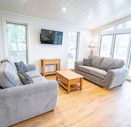 A living room with two grey sofas a wooden coffee table a wooden side table mounted television lamp and large windows at Bluebell Lodge in Gargrave