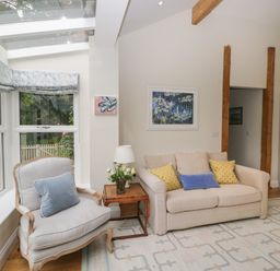 A living room with a beige sofa yellow and blue pillows a light blue cushioned armchair wooden side table with flowers and a lamp at The Roost in Cheriton near Alresford