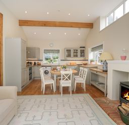A kitchen and dining area with a round table and chairs next to a wood burning stove at The Roost in Cheriton near Alresford